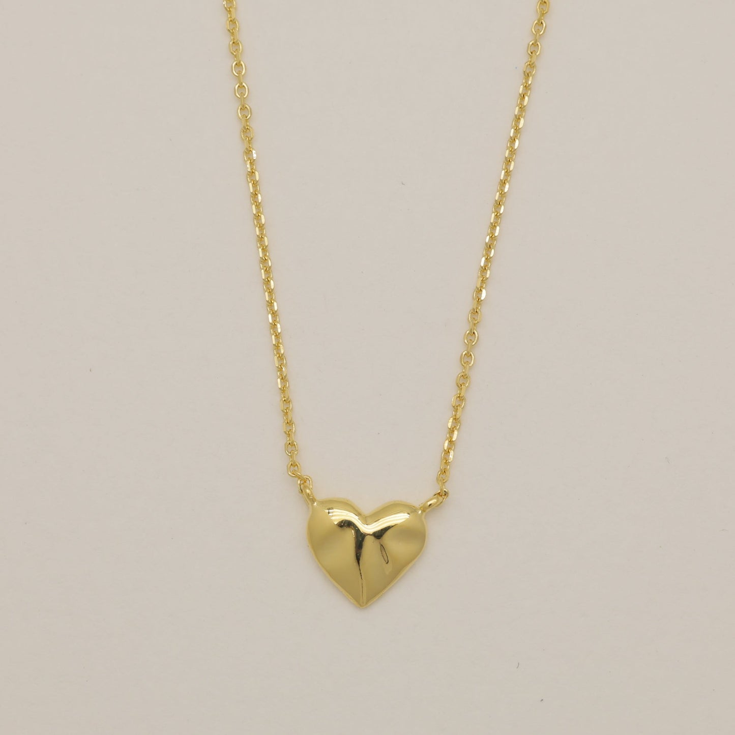 Gold heart-shaped pendant necklace on a beige background