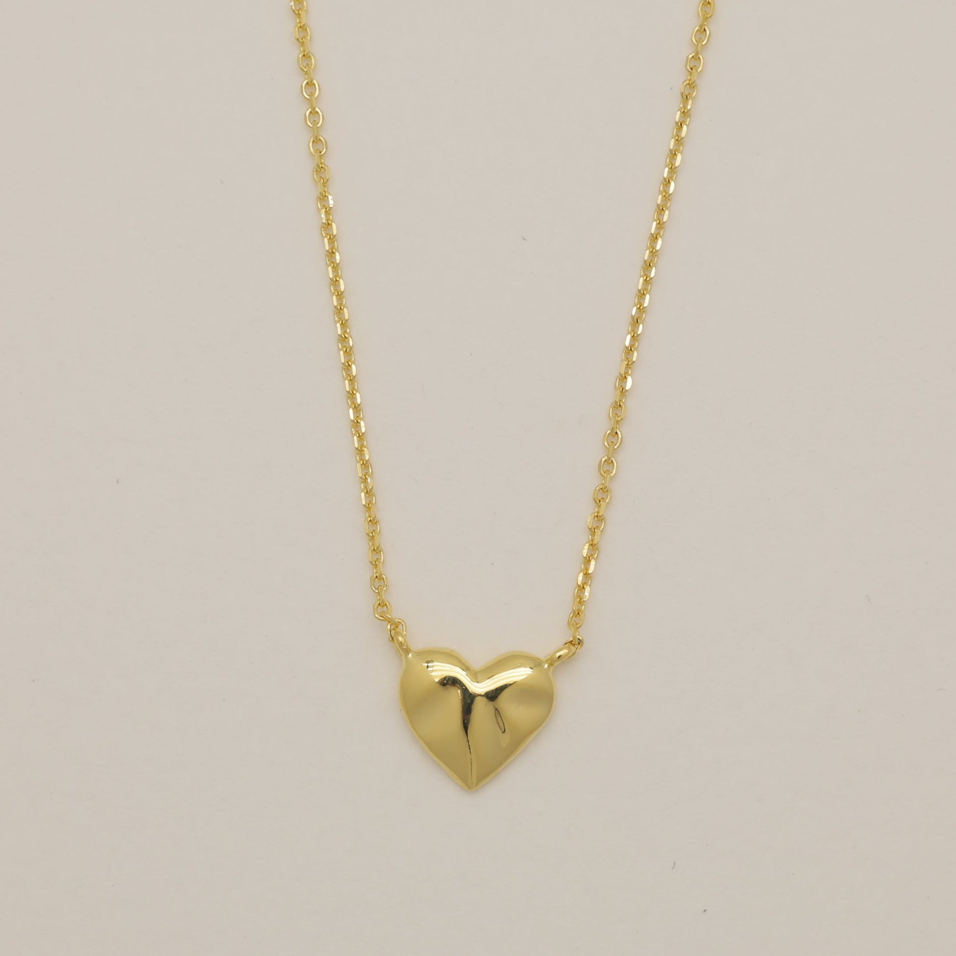 Gold heart-shaped pendant necklace on a beige background