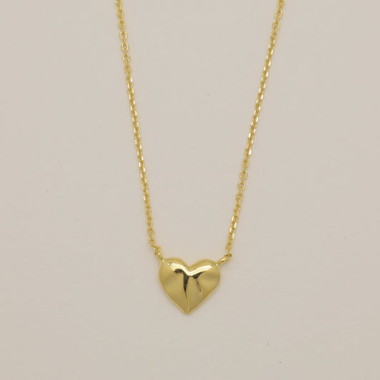 Gold heart-shaped pendant necklace on a beige background