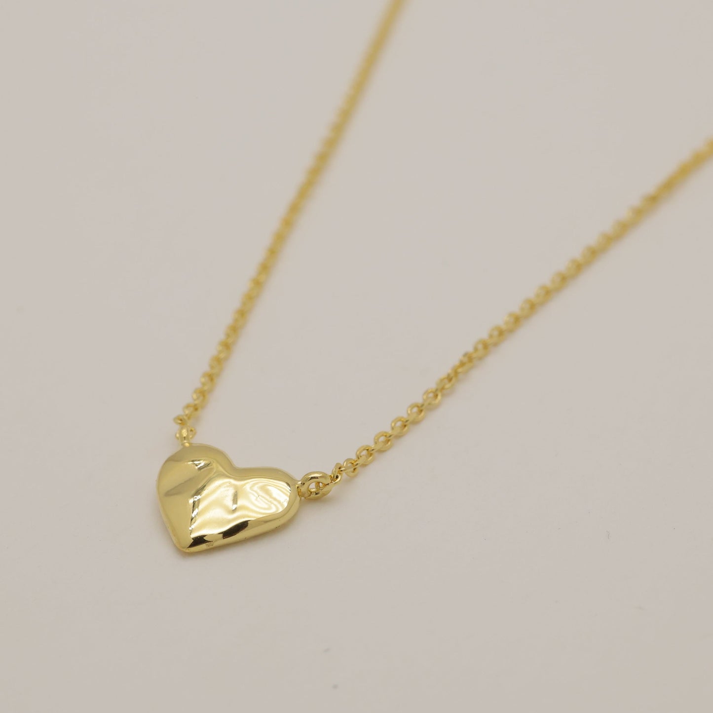 Gold heart-shaped pendant necklace on a light gray background
