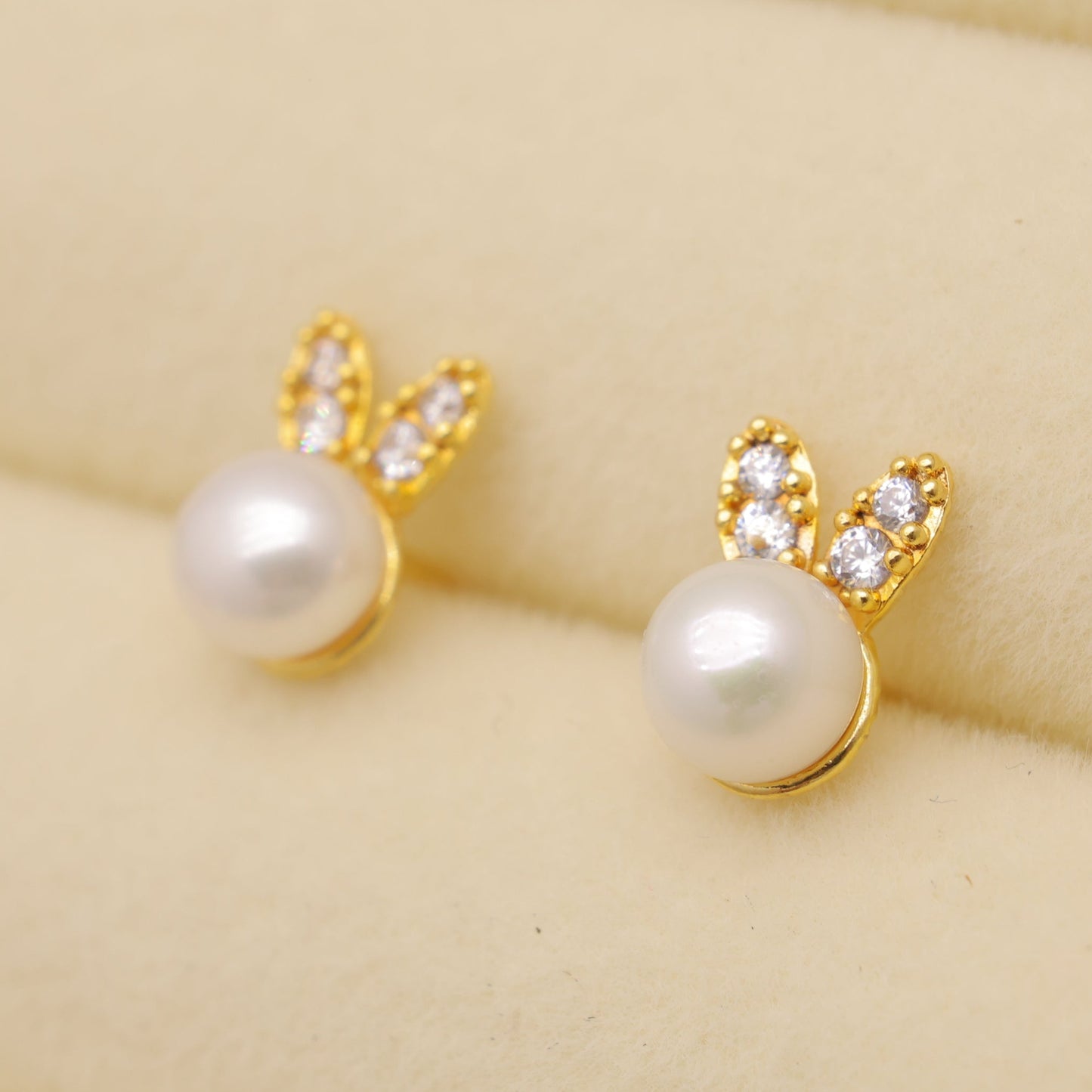 Gold earrings with pearl-like beads on a beige background