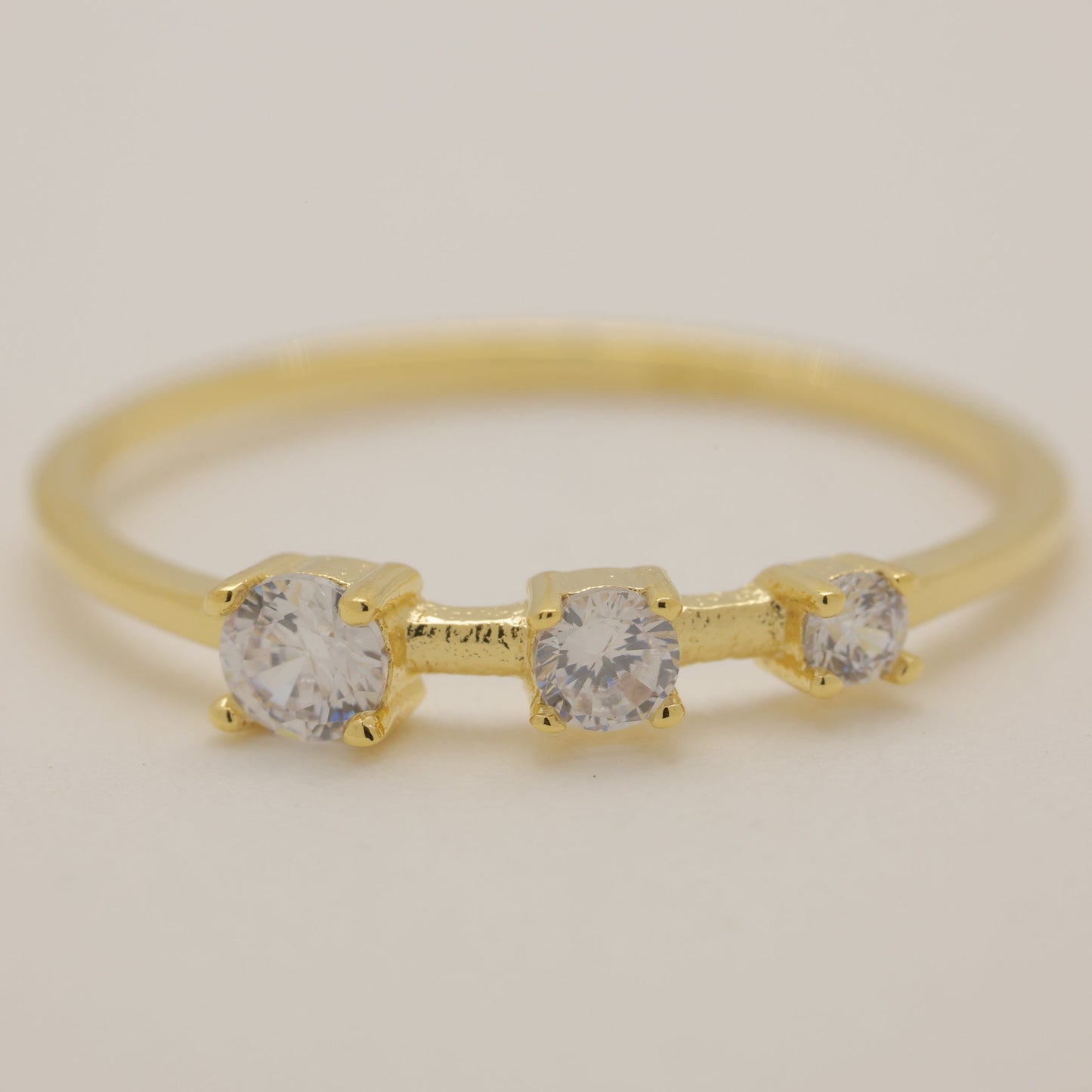 Gold ring with three clear gemstones on a beige background