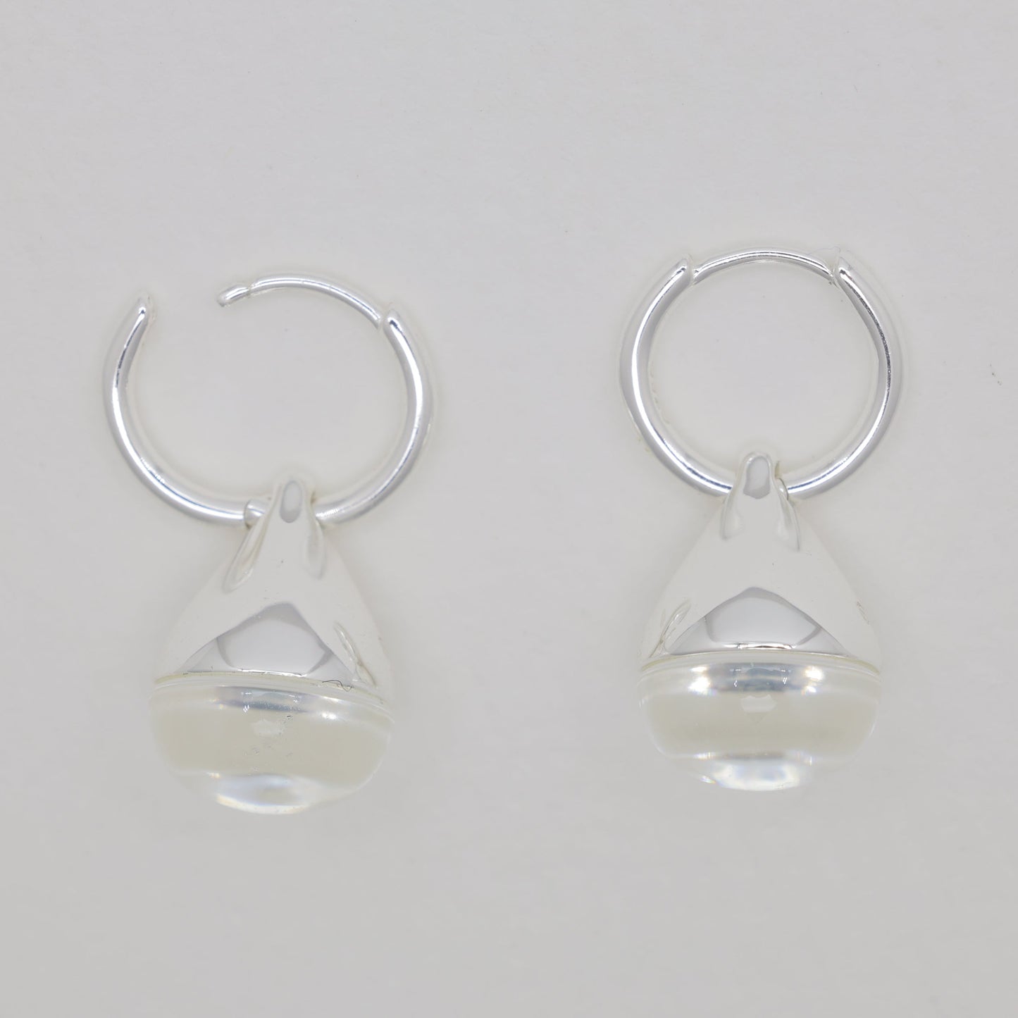 Pair of silver hoop earrings with clear teardrop-shaped charms on a light gray background