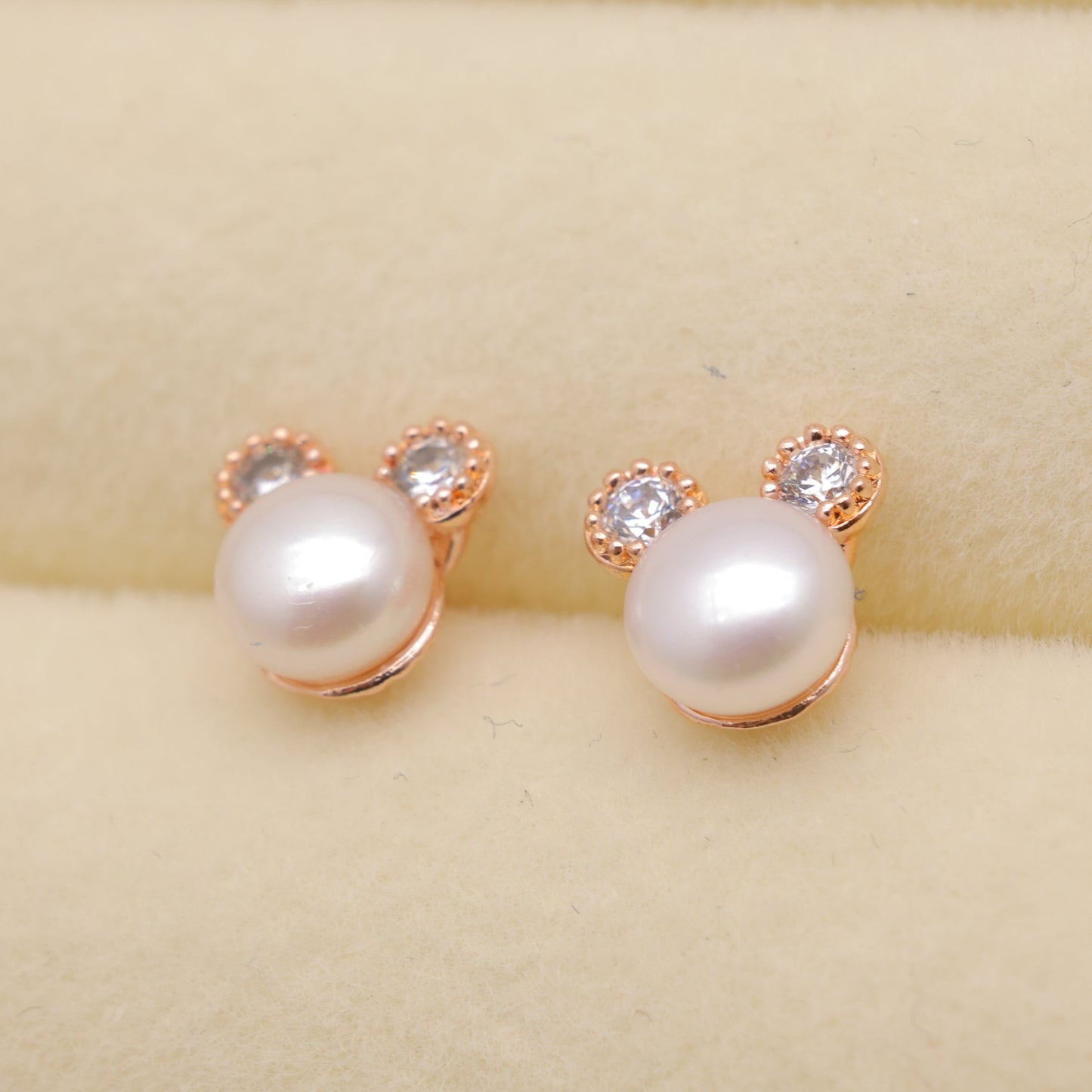 Pearl earrings with rose gold accents on a beige background