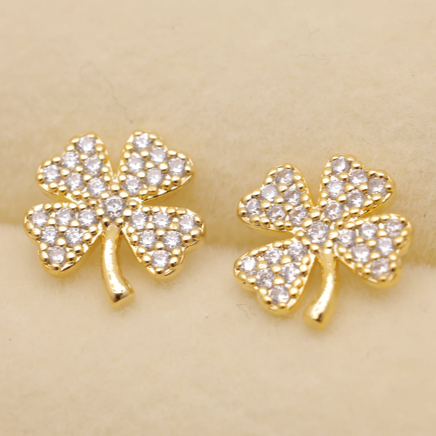 Gold four-leaf clover earrings with clear stones on a beige background