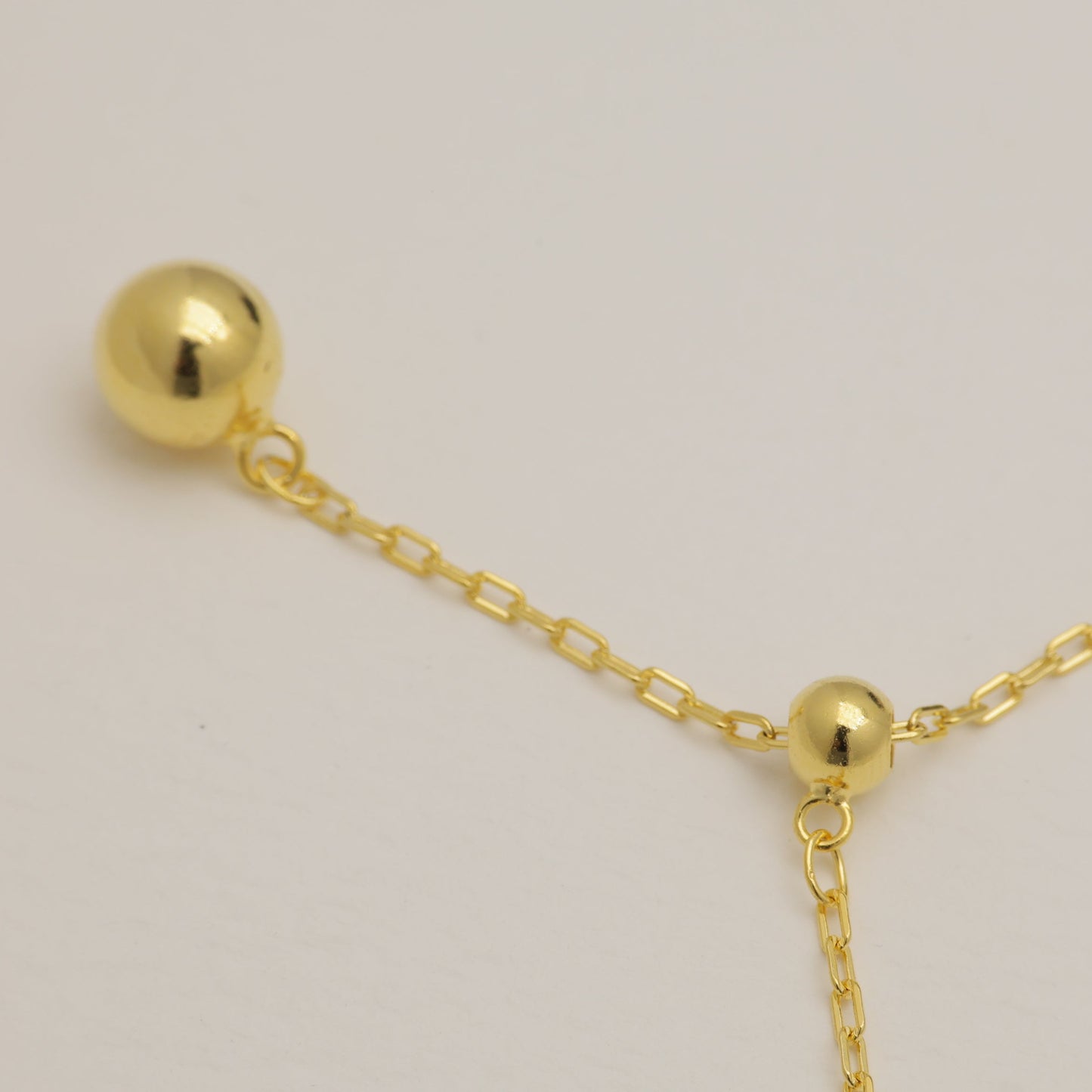 Gold necklace with two spherical pendants on a light gray background