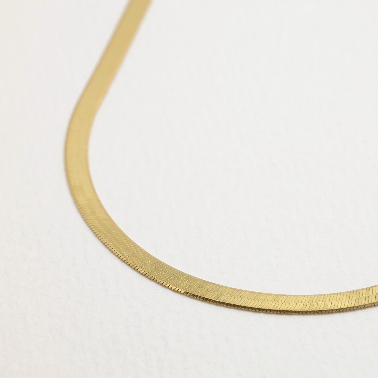 Close-up of gold vermeil herringbone necklace laid flat on a soft white surface