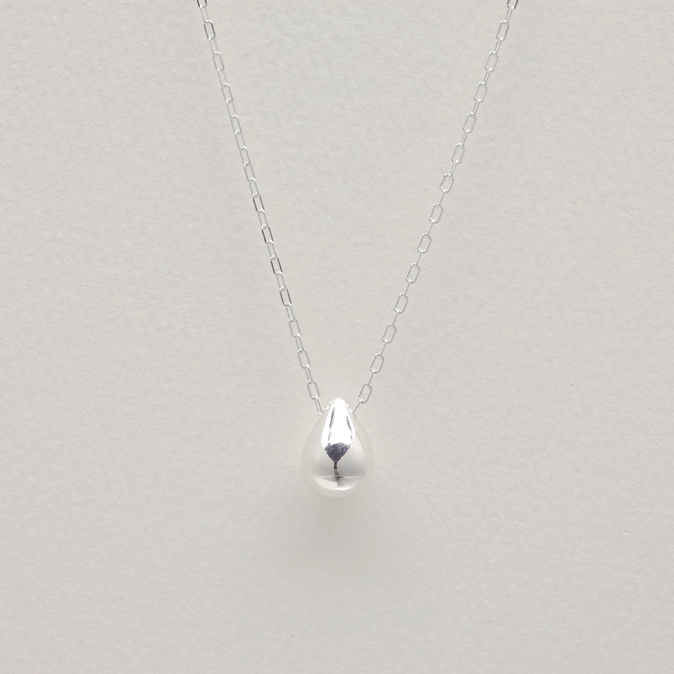 Long sterling silver necklace with teardrop pendant on white background – minimalist sculptural jewelry design.