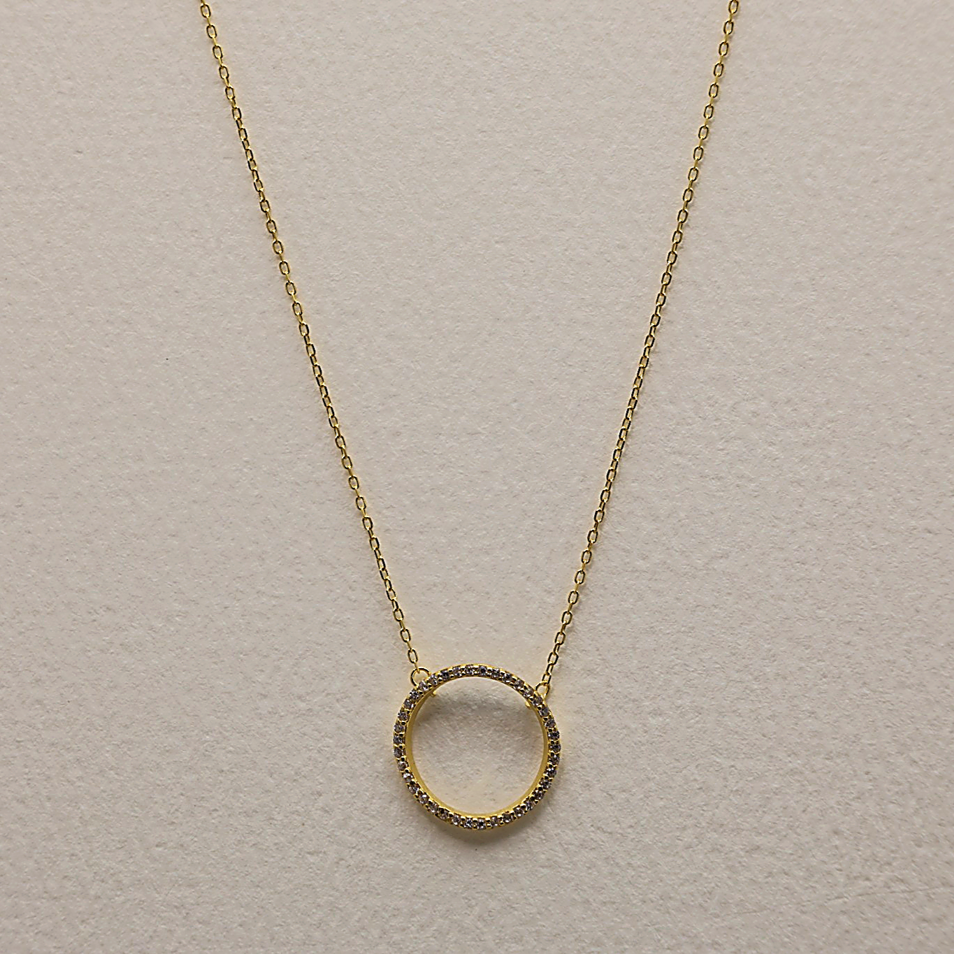Close-up of gold vermeil necklace with open circle pendant set with cubic zirconia, shown on light background
