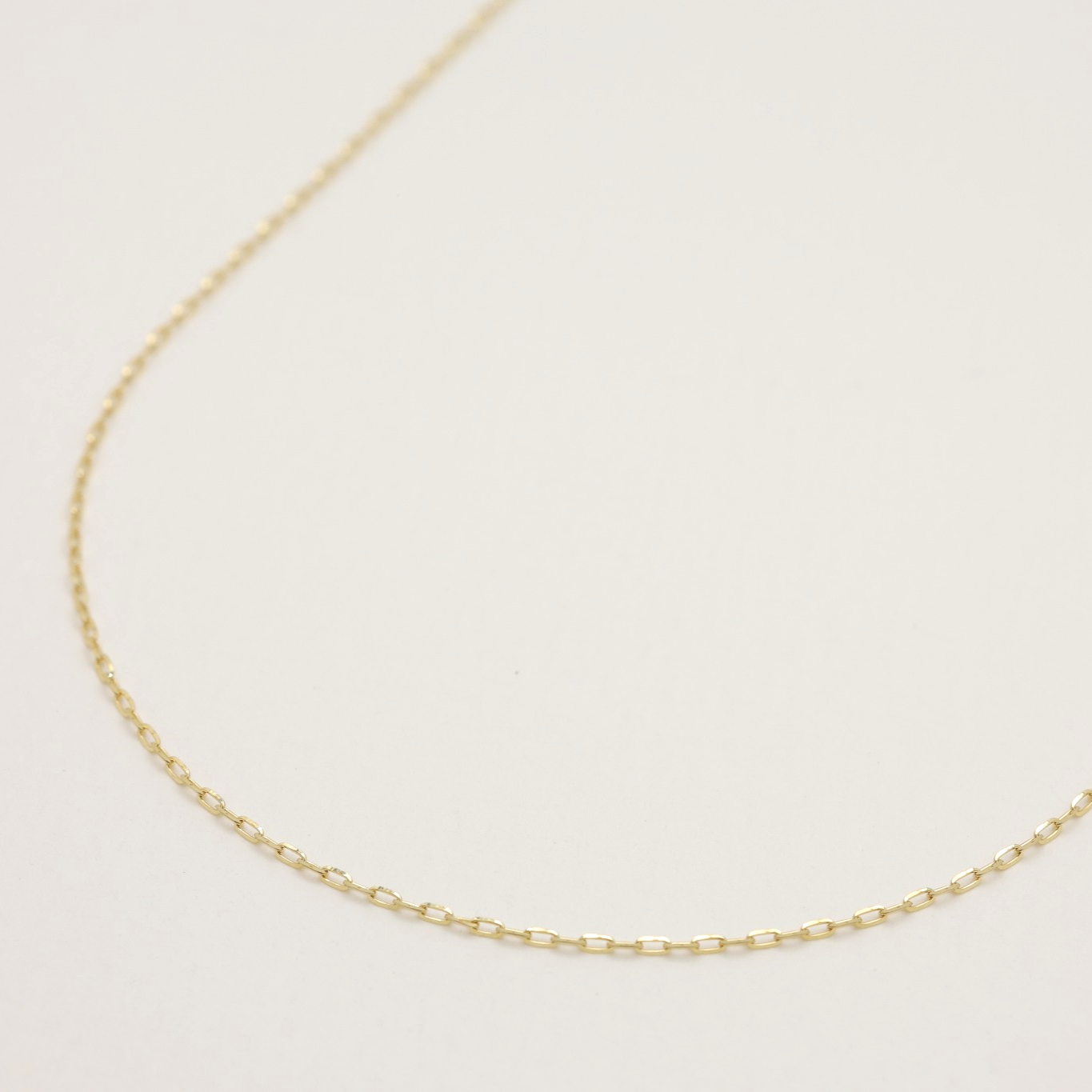 Close-up of 10K gold rectangular link chain necklace on light background, showing fine details