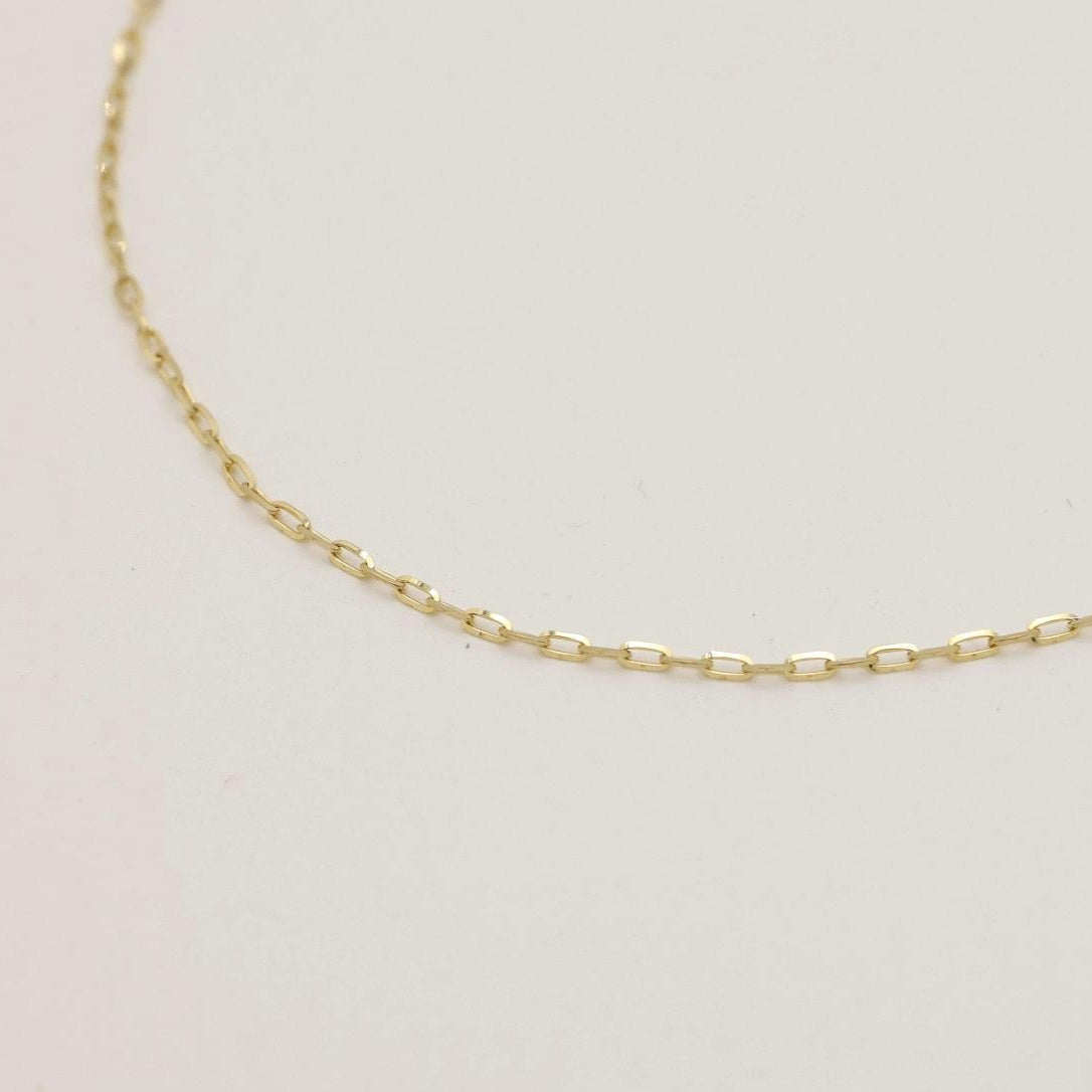 A close-up view of a delicate 10K gold chain bracelet with oval links, softly curved on a neutral surface.