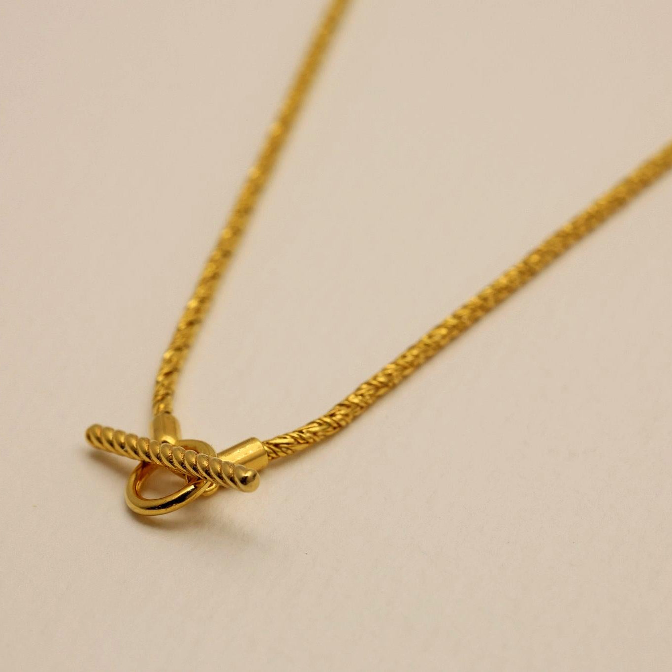 Front curve of the Érine Necklace with focus on the textured gold vermeil chain against a light beige surface.