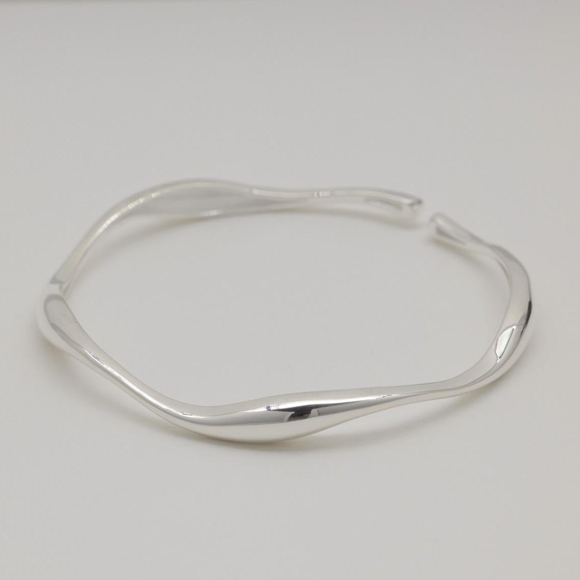Image 1: Sculptural sterling silver cuff bracelet with fluid curves, displayed on a soft white background.