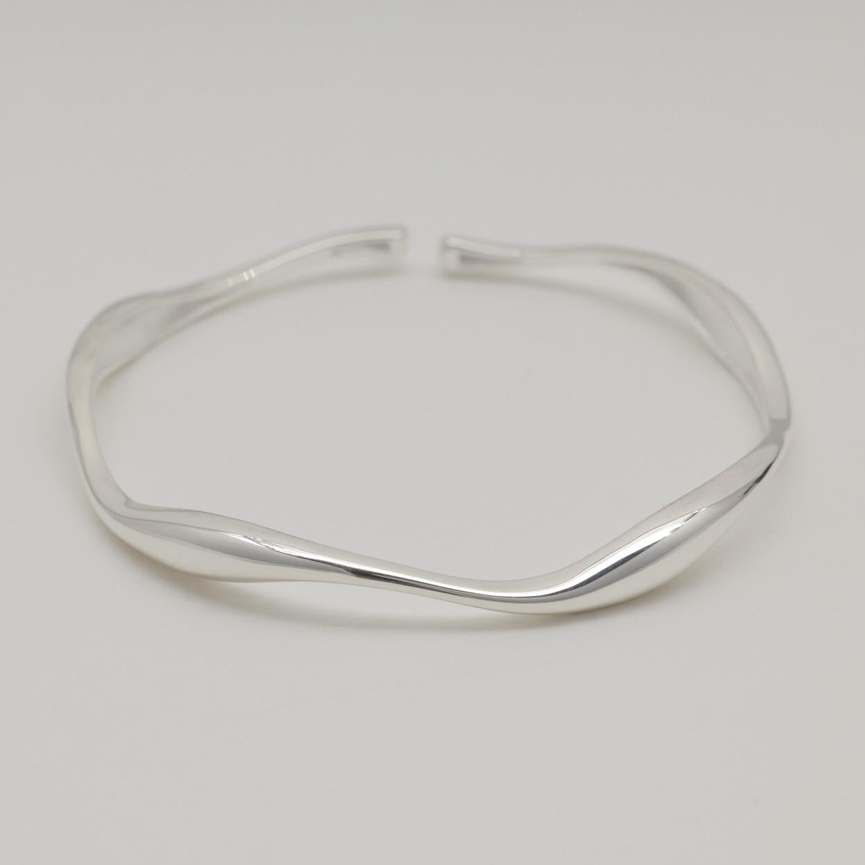 Image 1: Sculptural sterling silver cuff bracelet with fluid curves, displayed on a soft white background.