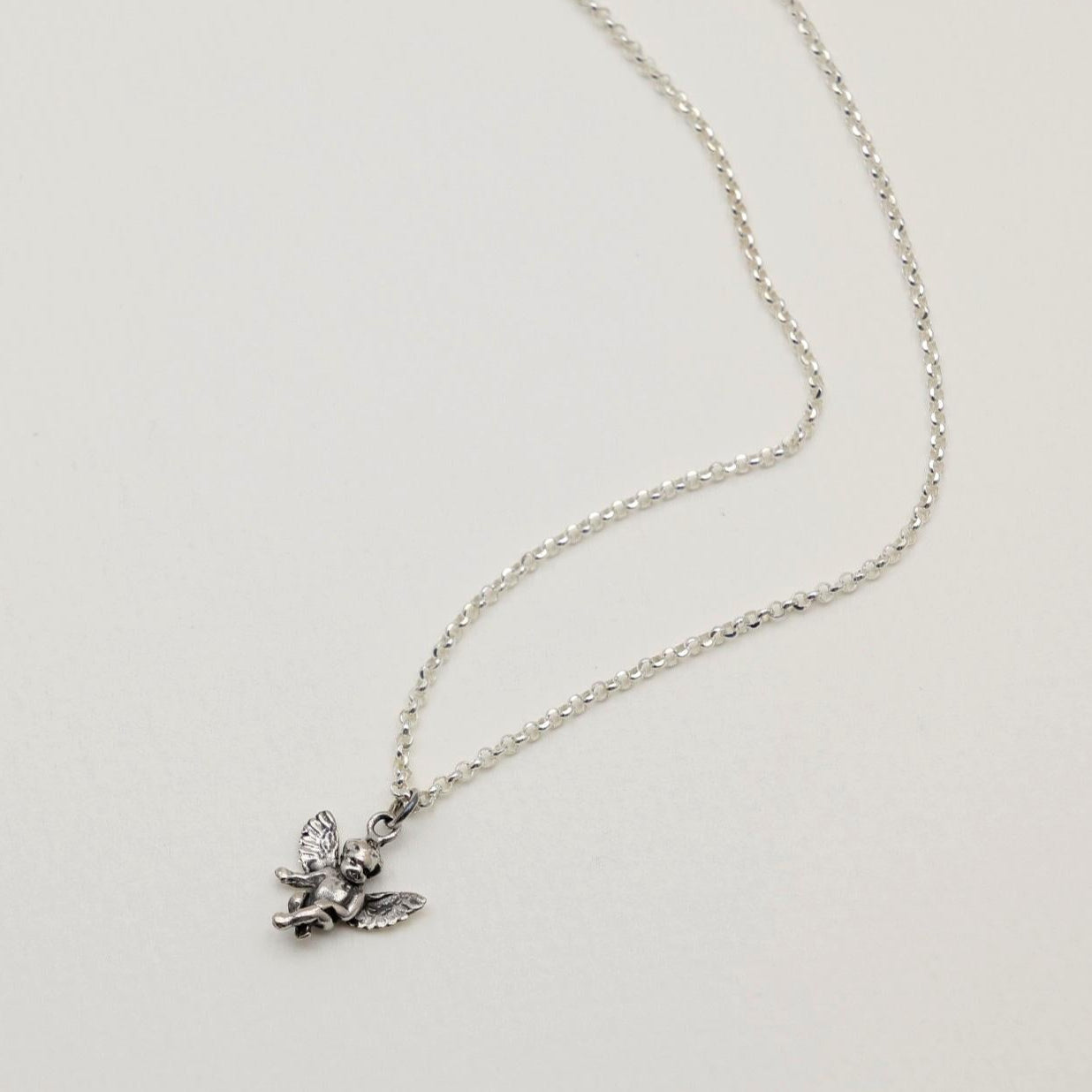Sterling silver pendant in the shape of a seated cherub angel with wings, oxidized antique finish, photographed on a neutral background