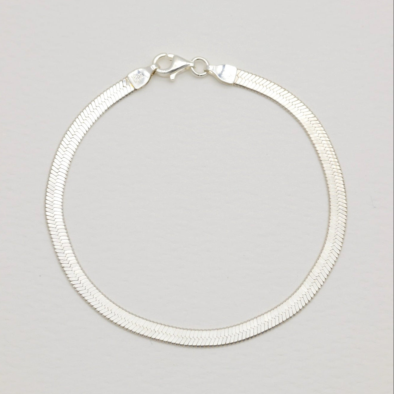 Flat herringbone bracelet in polished sterling silver with lobster clasp.