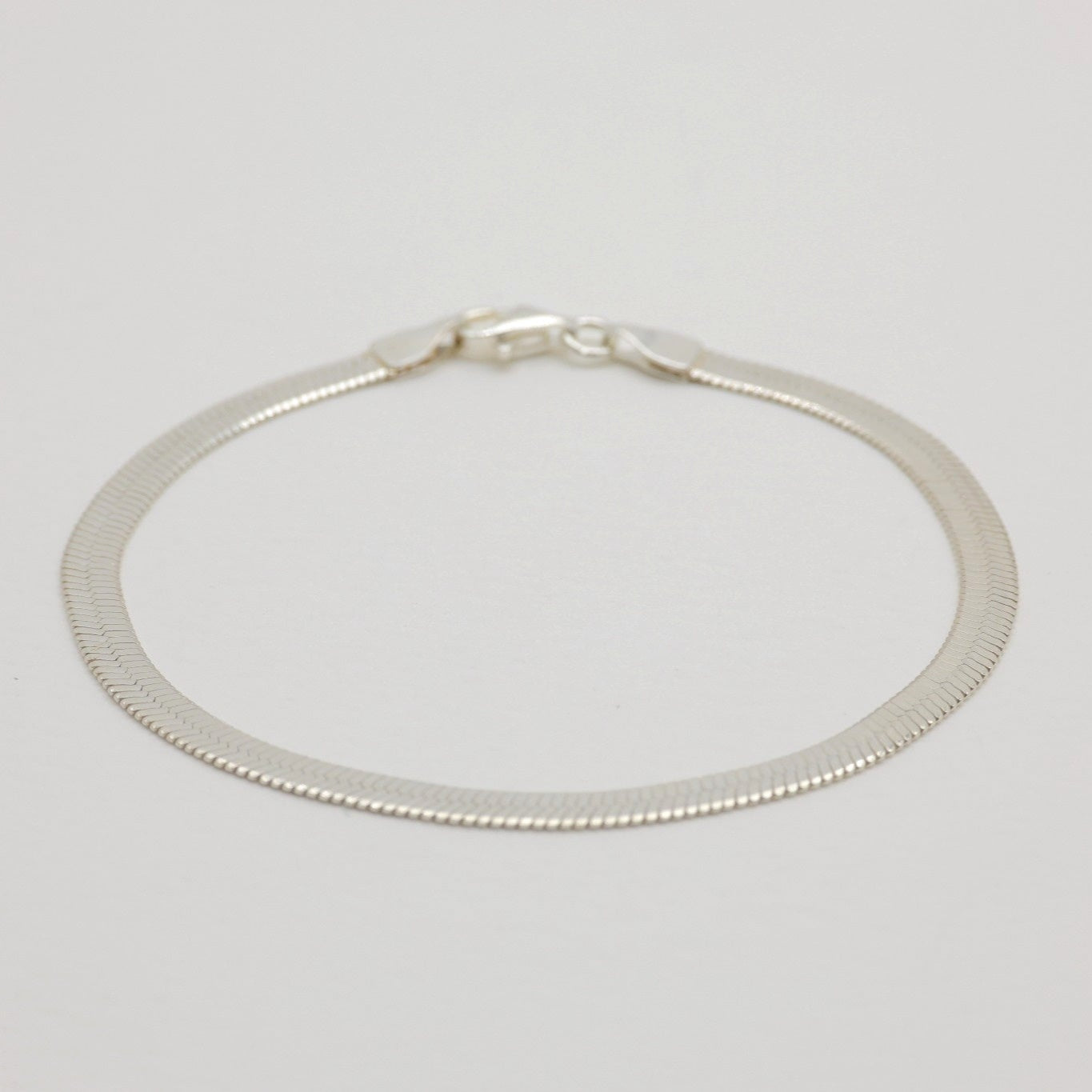 Flat herringbone bracelet in polished sterling silver with lobster clasp.