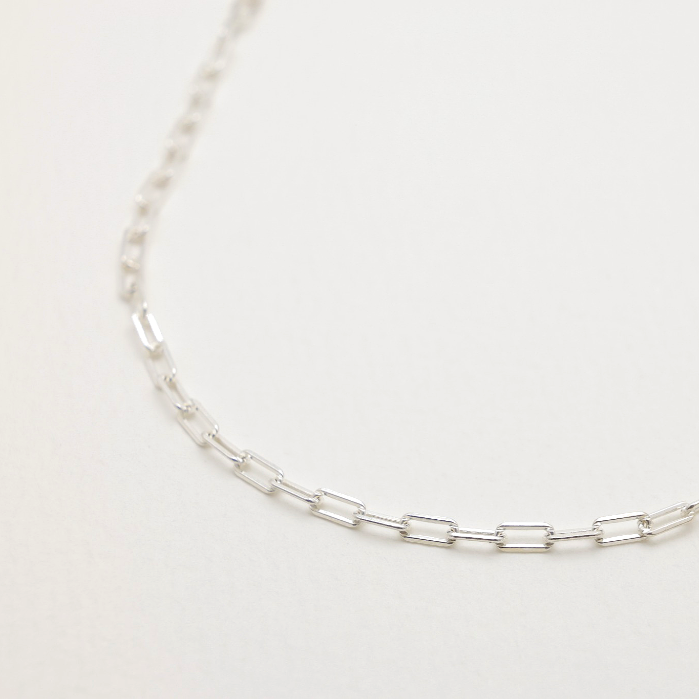 Close-up of sterling silver rectangular link chain necklace on neutral background