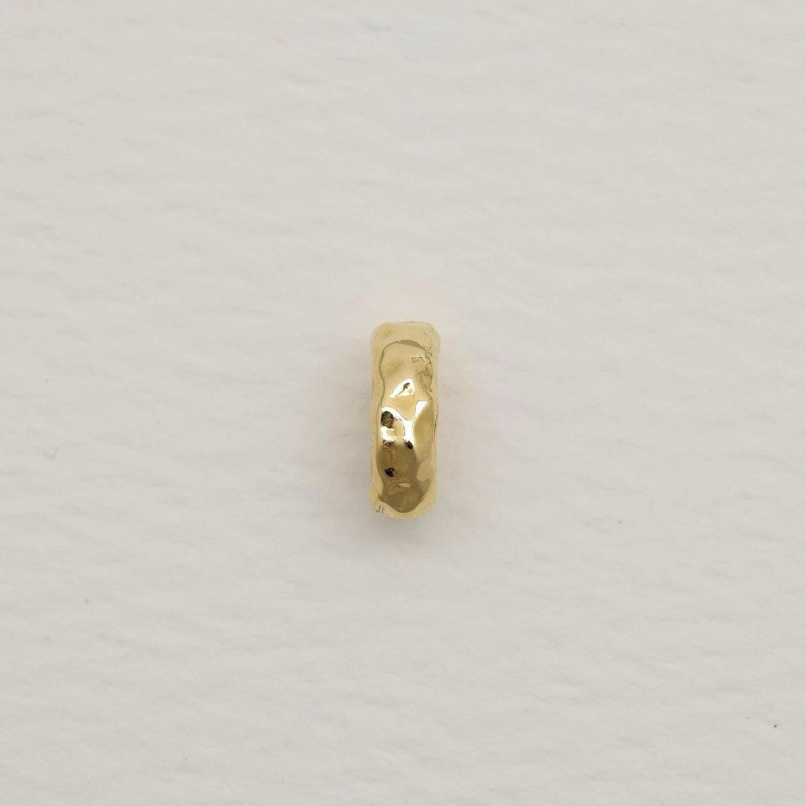 14K gold organic oval charm with hammered finish, photographed on soft white textured paper background