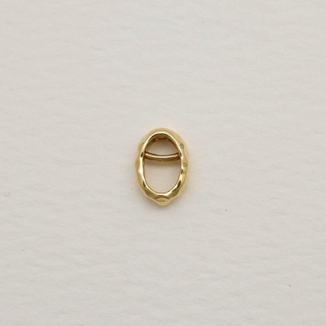 14K gold organic oval charm with hammered finish, photographed on soft white textured paper background