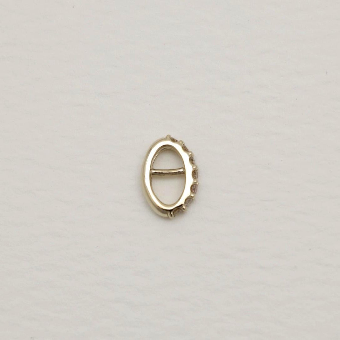 14K gold oval charm with natural pavé diamonds along one edge, photographed on a soft white background.