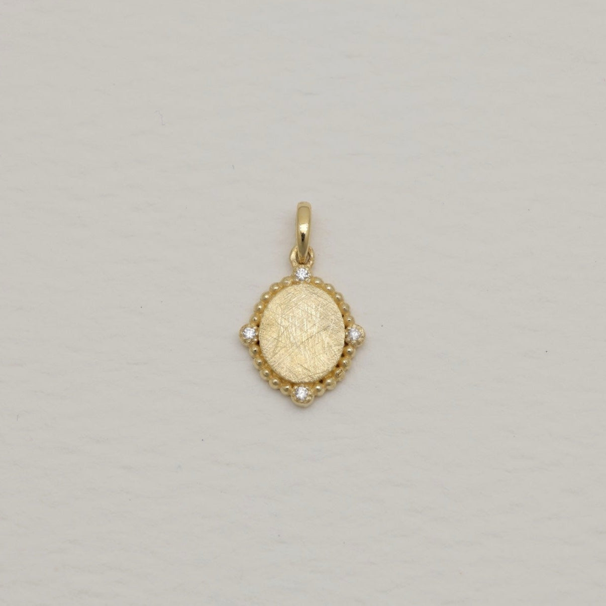 14K gold charm pendant with oval brushed center and four cubic zirconia, surrounded by beaded details.