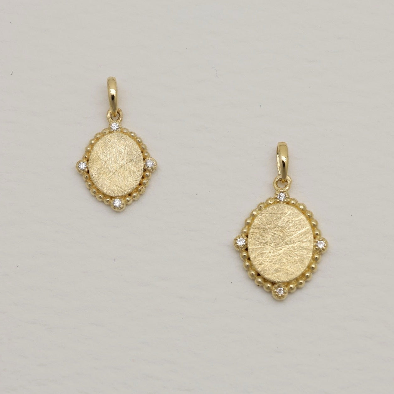 14K gold charm pendant with oval brushed center and four cubic zirconia, surrounded by beaded details.