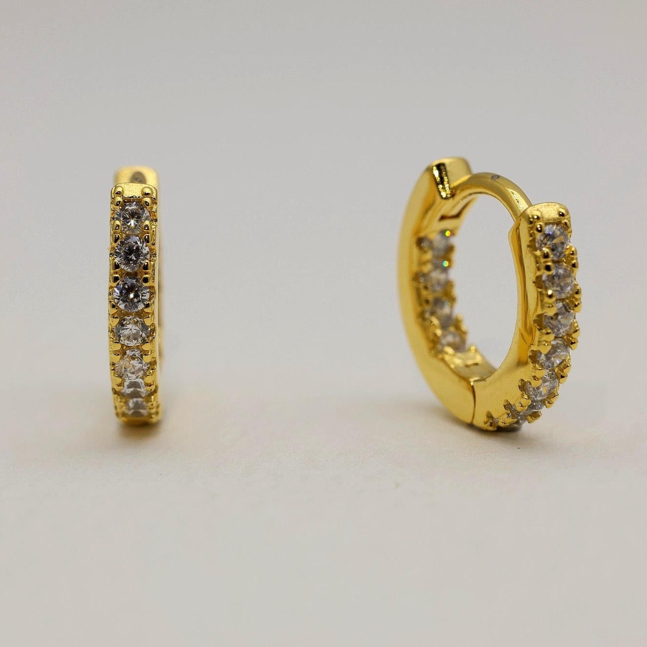 Close-up of gold vermeil pavé huggie earrings with cubic zirconia stones on neutral background