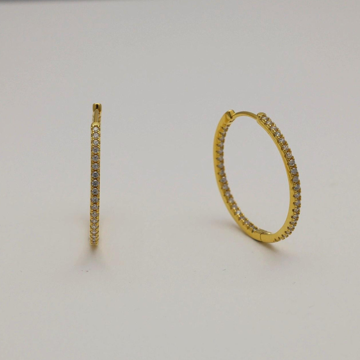 Close-up of gold vermeil pavé huggie earrings with cubic zirconia stones on neutral background