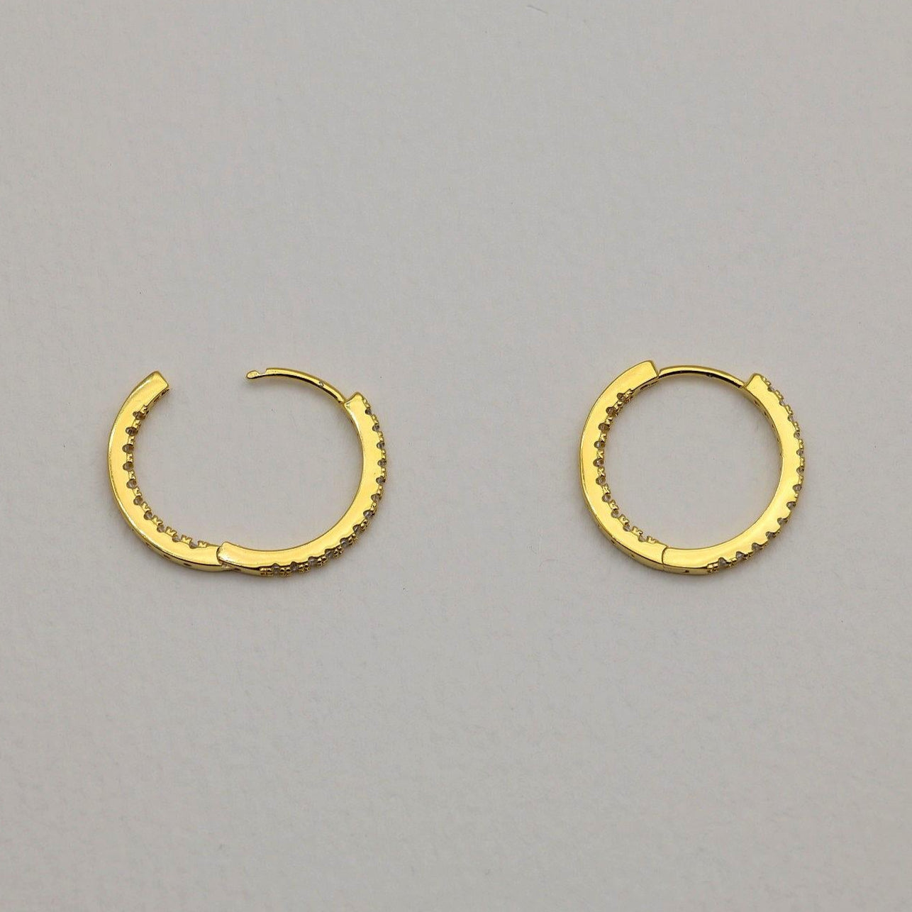 Close-up of gold vermeil pavé huggie earrings with cubic zirconia stones on neutral background
