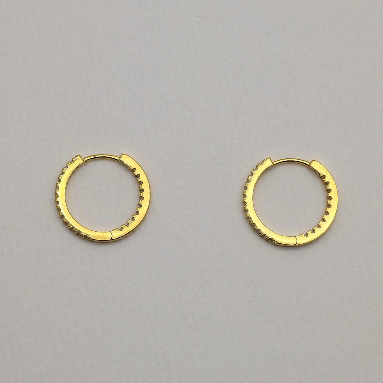 Close-up of gold vermeil pavé huggie earrings with cubic zirconia stones on neutral background
