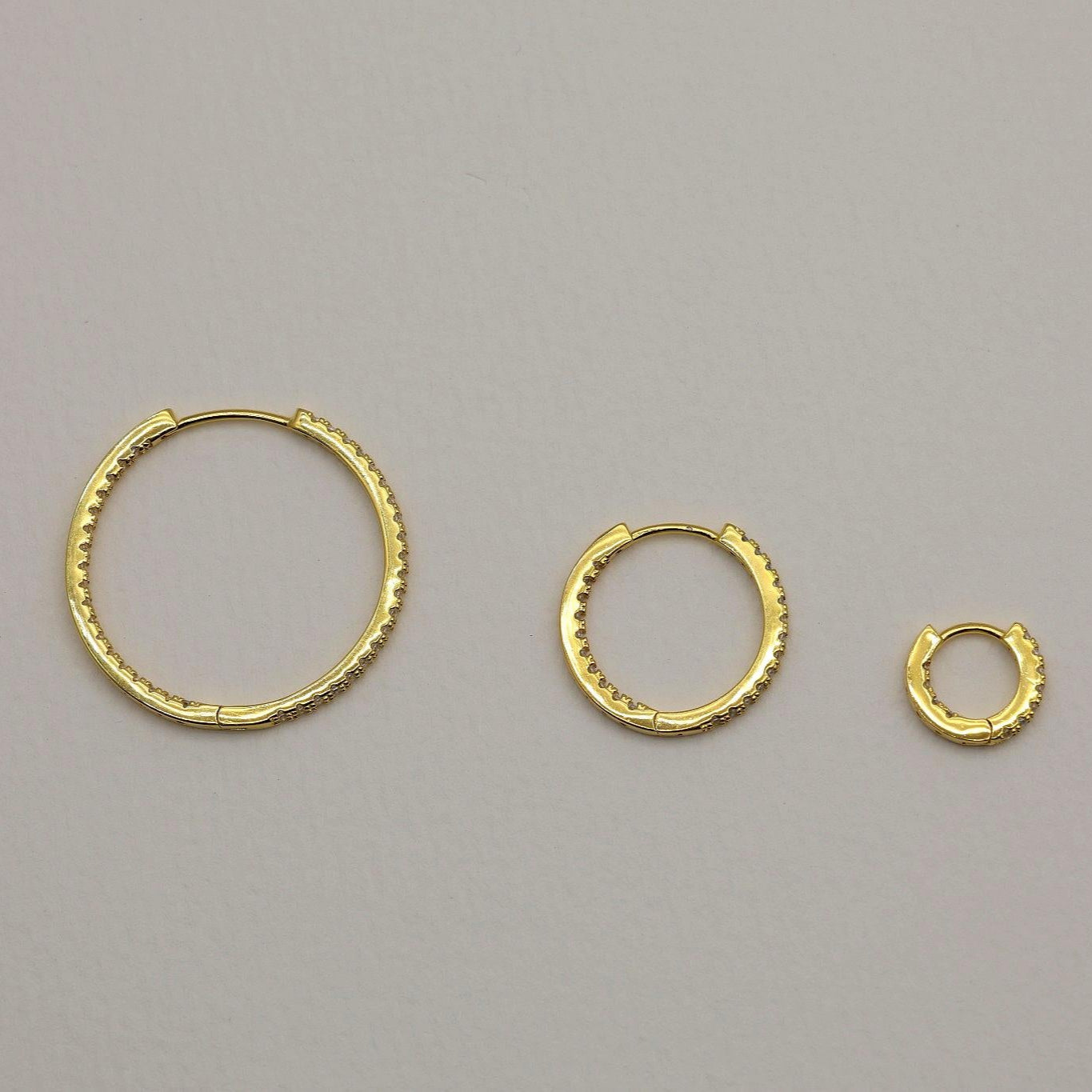 Close-up of gold vermeil pavé huggie earrings with cubic zirconia stones on neutral background
