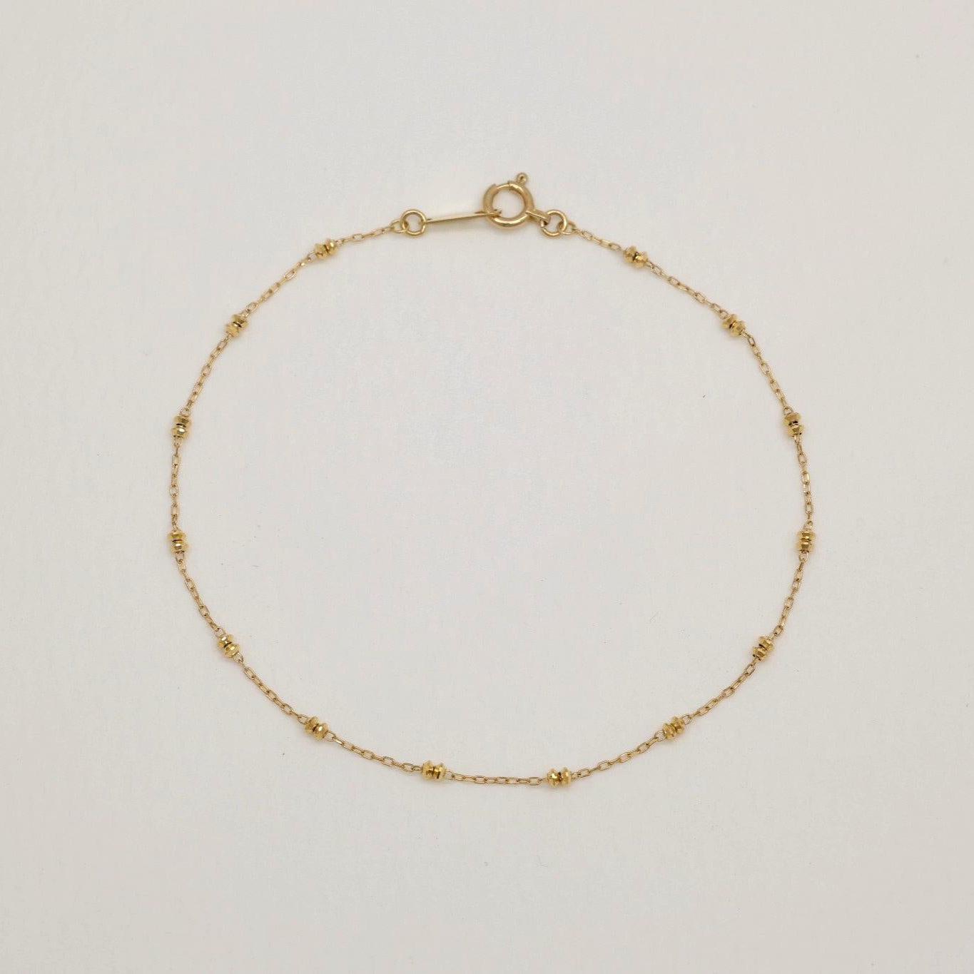 Delicate 10K gold bracelet with polished bead details, 18cm in length, laid flat in a circular shape on a light background.