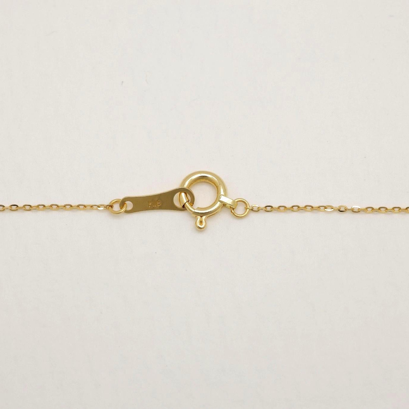 Close-up of 18K gold necklace with Akoya pearl and natural diamond pendant on a light background.