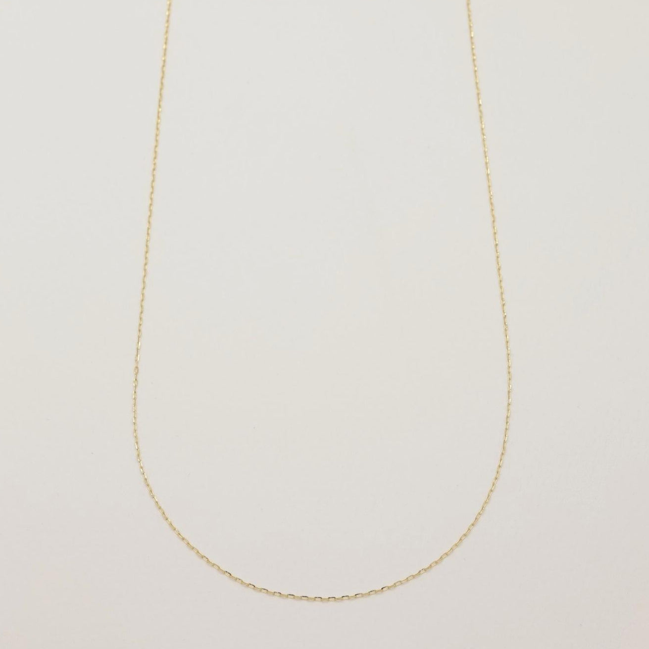 Full view of the Juliette Chain Necklace in 10K gold laid flat in a subtle curve on a neutral background.
