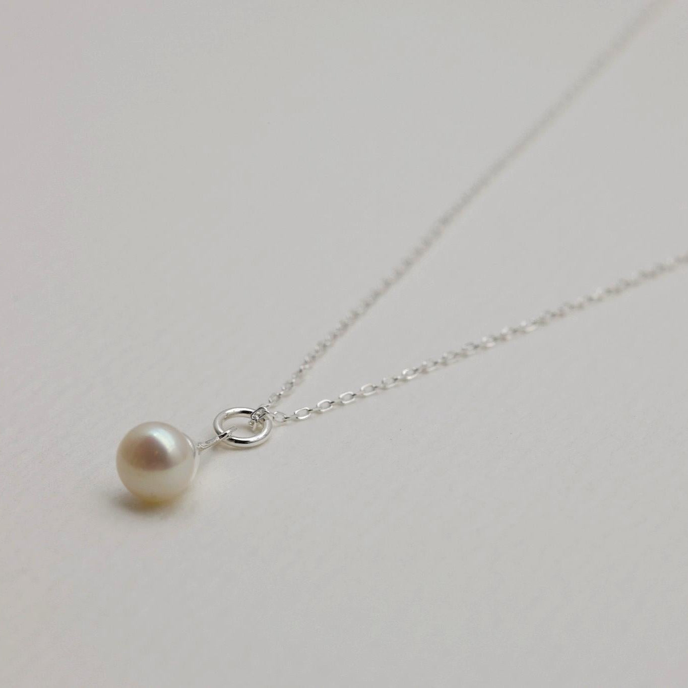 Close-up of the dangling natural pearl pendant on the fine silver chain of the Léa Necklace.