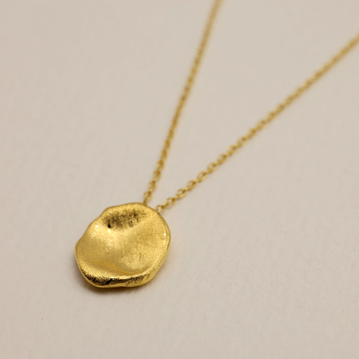 Organic, hand-textured gold vermeil disc pendant of the Léontine Necklace against a white backdrop.