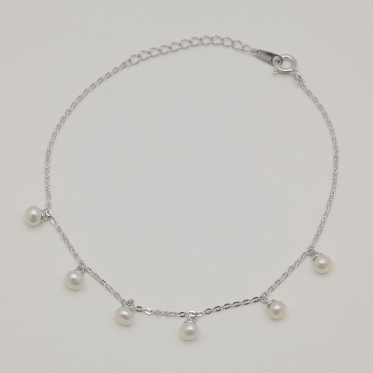 Sterling silver chain bracelet with six small natural pearl drops, photographed flat on a neutral background.