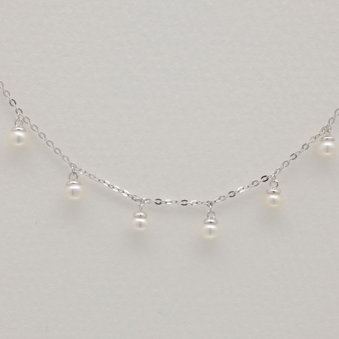 Sterling silver chain bracelet with six small natural pearl drops, photographed flat on a neutral background.