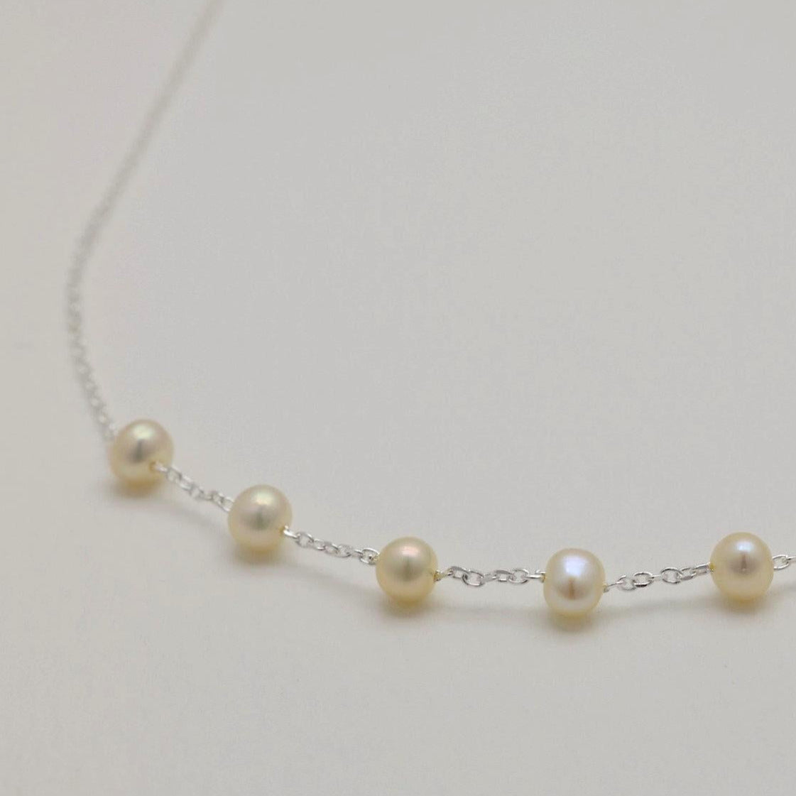 Close-up of natural pearls spaced along the fine silver chain of the Vivienne Necklace.