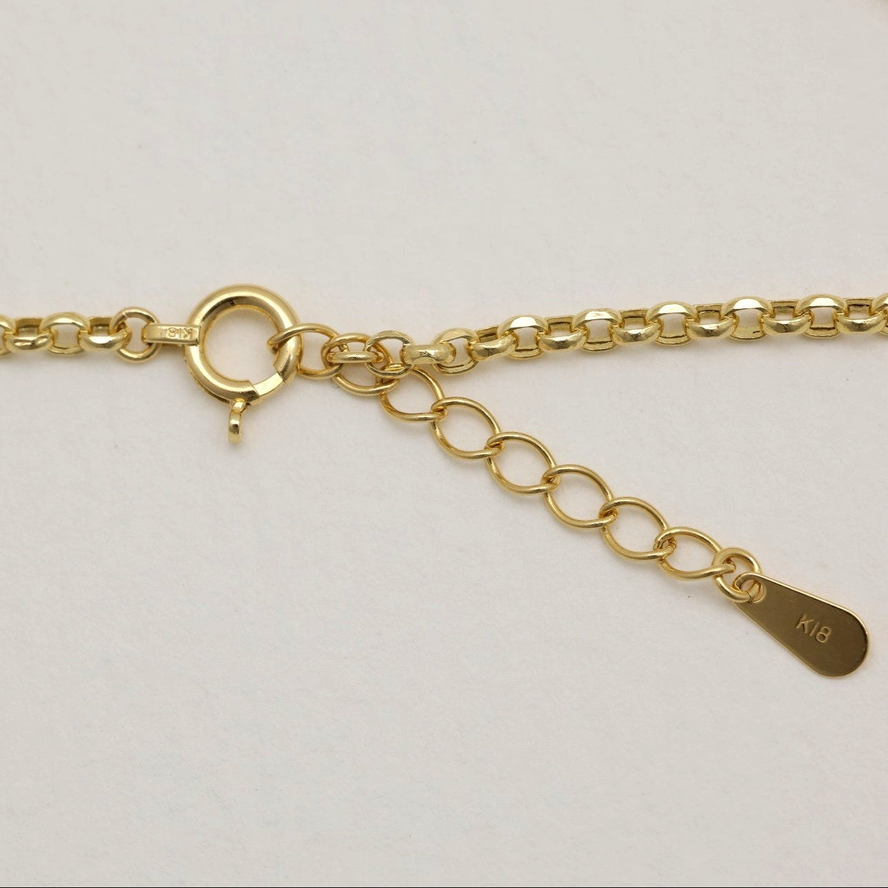 Close-up of 18K gold spring clasp and tag engraved “K18” on polished chain bracelet