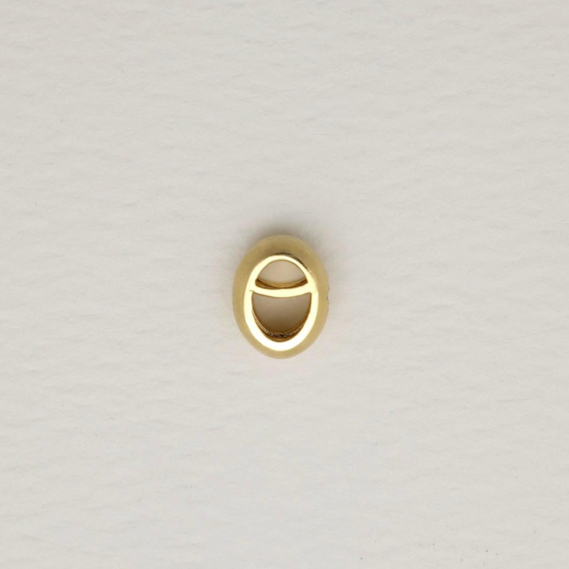Gold oval pendant with a matte finish and engraved starburst set with a tiny diamond, photographed on a soft white background.