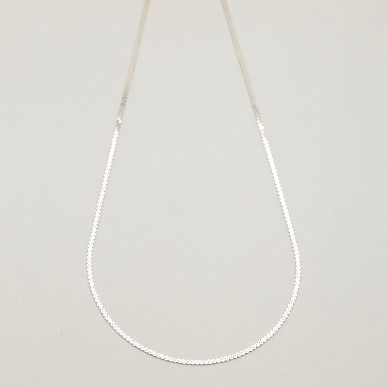 Flat lay of the Delia Chain Necklace in 925 sterling silver, showcasing its fine circular links.