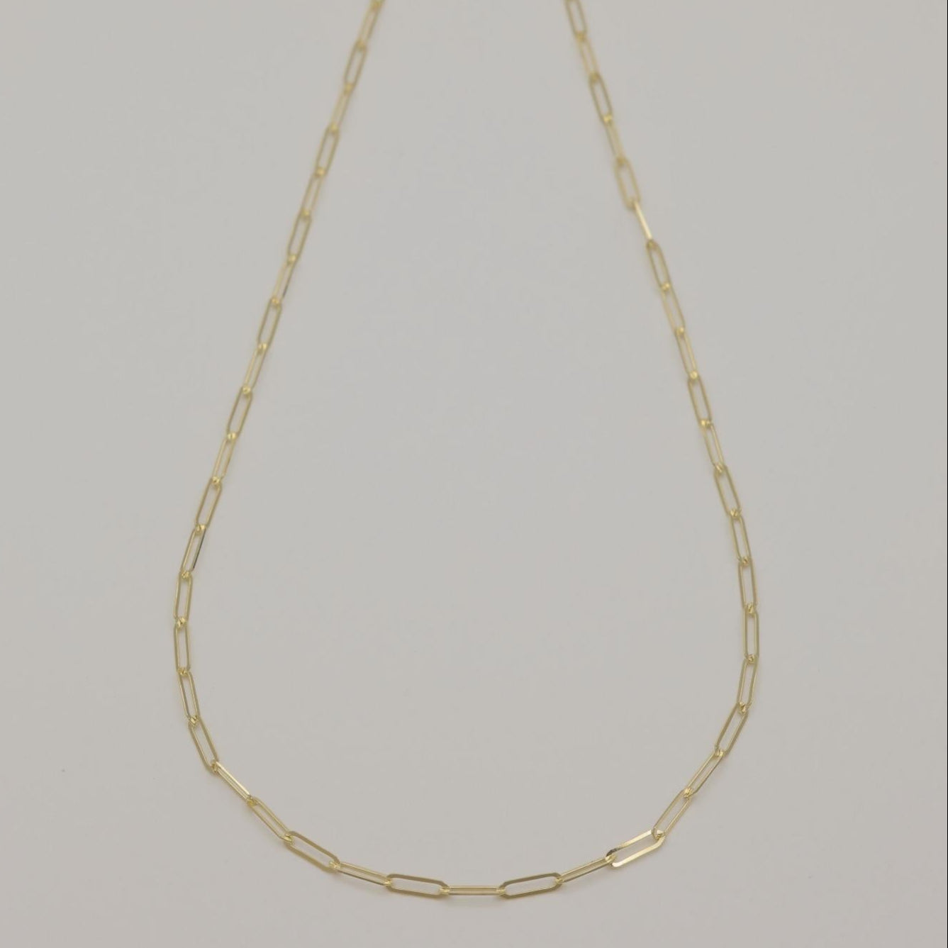 14K gold fine chain necklace displayed in a gentle curve on cream fabric background