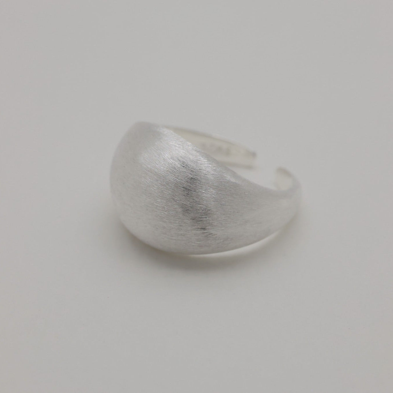 Angled lifestyle shot of brushed silver dome ring on neutral background