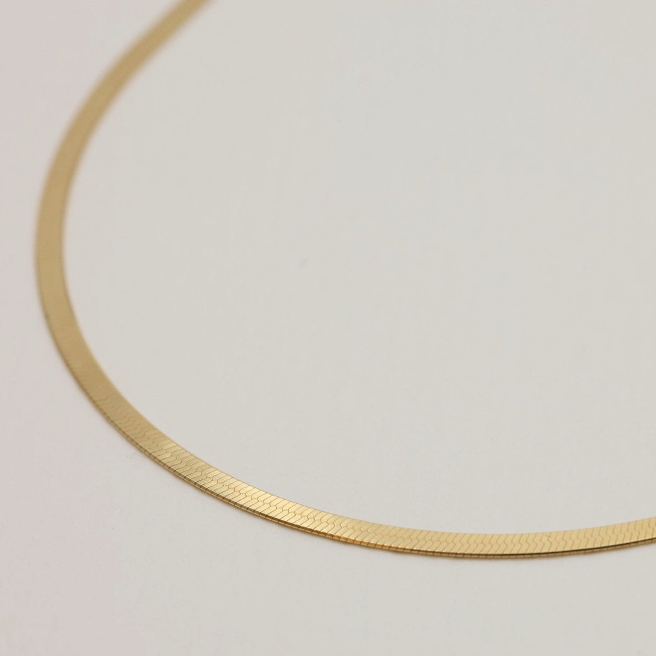 Close-up of the flat snake-chain links of the Odette Necklace in 14K Gold, highlighting the reflective polished surface.