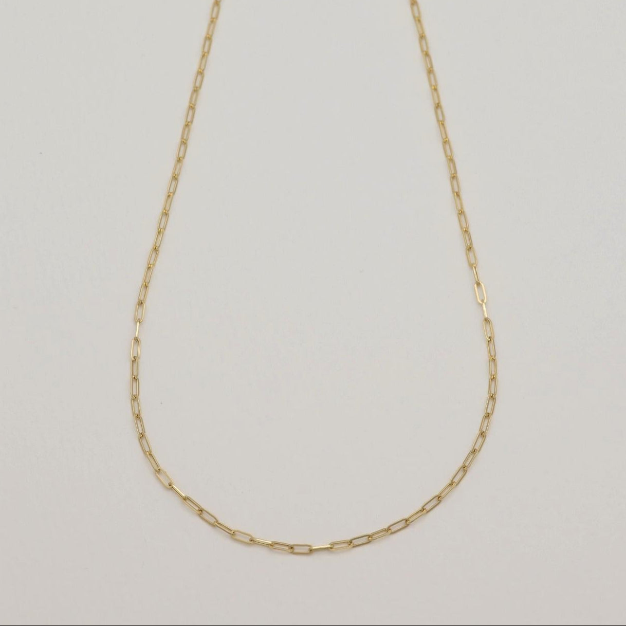 Minimalist 18K gold chain necklace shown in full length, styled in a curve.