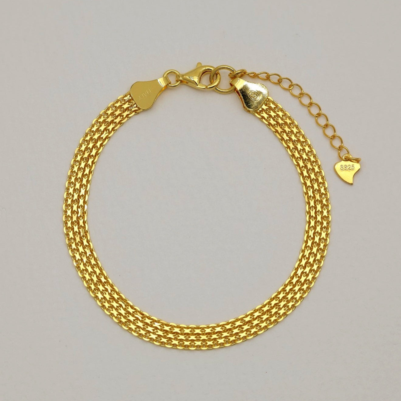 Gold vermeil mesh bracelet arranged in a full circle on a neutral background, showcasing its polished woven texture and lobster clasp with heart tag extender.