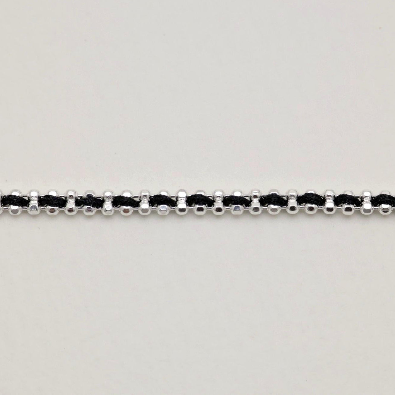Detailed shot of the black thread woven between polished silver links in the bracelet.