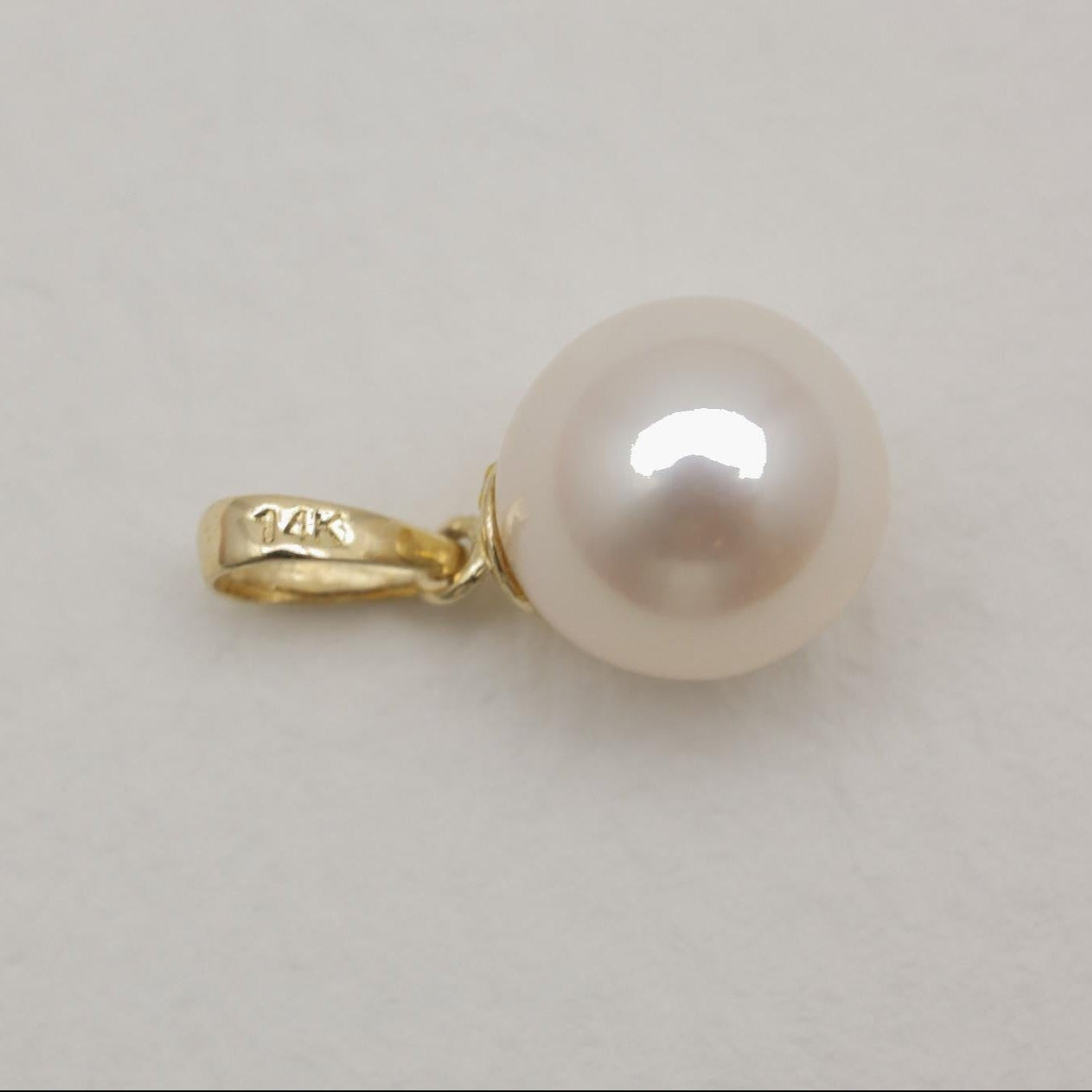 Close-up of natural pearl pendant with 14K gold bail on soft background